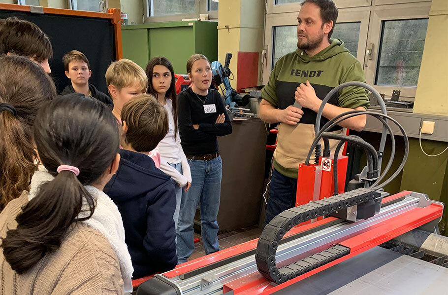 Schülerinnen und Schüler beobachten die automatisierte Arbeitsweise einer CNC-Maschine in der Metallwerkstatt